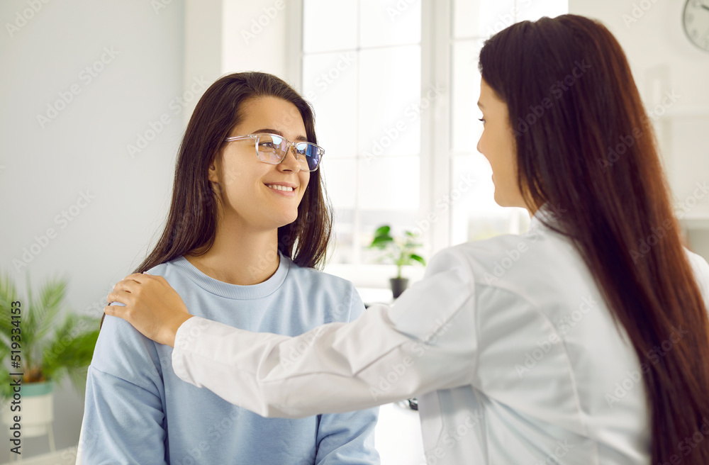 Cheerful young woman patient consults with professional doctor working in hospital smiling looks at therapist and listens to recommendations for treatment sits in bright office of modern clinic