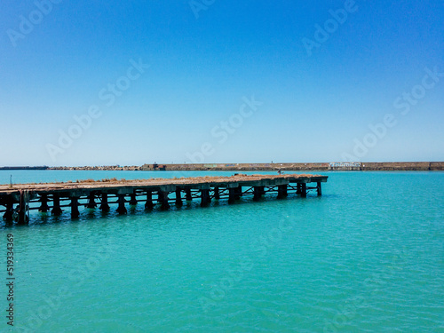 An old pier in turquoise sea water under a blue cloudless sky.