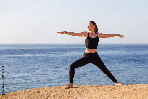 Young fitness woman performing warrior yoga pose at the beach in the morning