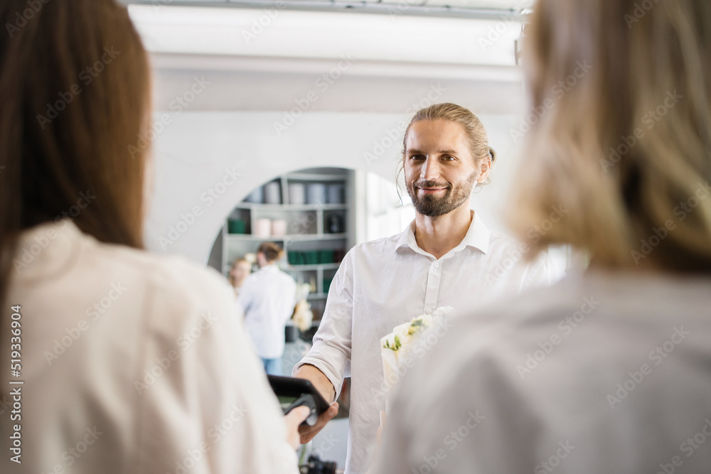 Attractive young bearded man shopping and paying with electronic credit card in his smartphone using app in flower shop. Attractive young bearded man shopping and paying with electronic credit card in his smartphone using app in flower shop.