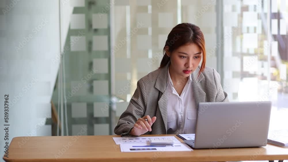 Business woman working in finance is calculating budget by calculator in bank office working while working on laptop and audit documents analyzing financial for accounting. Business woman working in finance is calculating budget by calculator in bank office working while working on laptop and audit documents analyzing financial for accounting.