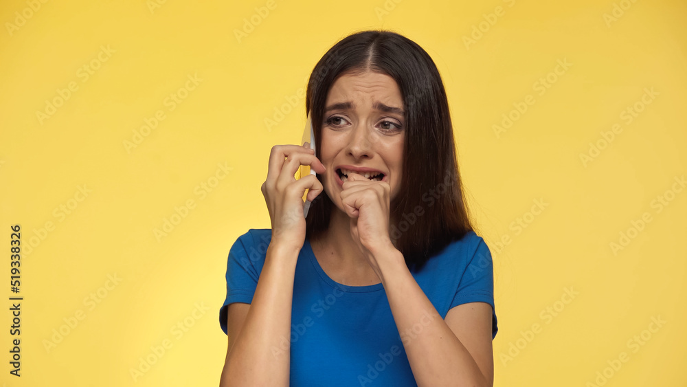 young brunette woman in blue t-shirt crying while talking on smartphone isolated on yellow. young brunette woman in blue t-shirt crying while talking on smartphone isolated on yellow.