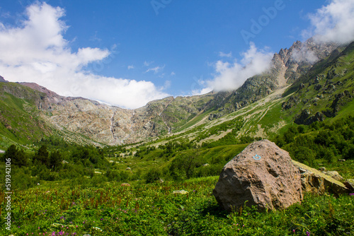 Mountain landscape with high stone cliffs and bright green grass on an alpine meadow in the Elbrus valley in the North Caucasus in Russia on a sunny summer day