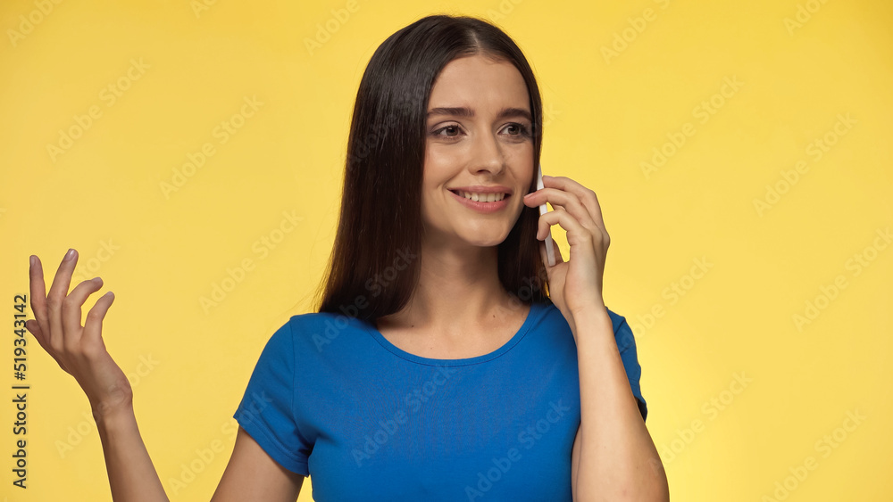 young happy woman in blue t-shirt talking on smartphone isolated on yellow.