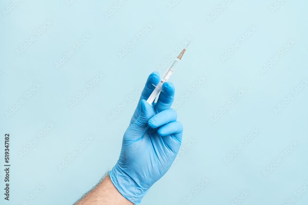 Close up picture of male hand with nitrile glove holding a syringe with vaccination on the blue background. Health care, vaccination cocncept. Close up picture of male hand with nitrile glove holding a syringe with vaccination on the blue background. Health care, vaccination cocncept.