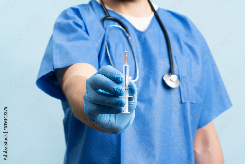 Close up picture of male doctor wearing medical scrubs and stethoskope over neck showing syringe full of vaccination. Close up picture of male doctor wearing medical scrubs and stethoskope over neck showing syringe full of vaccination.