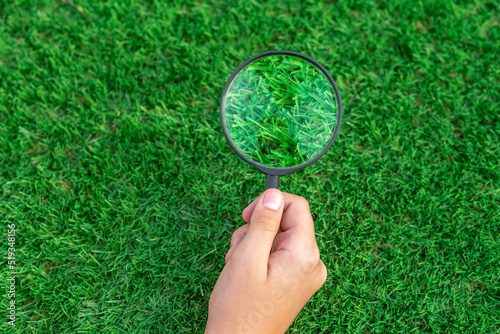 Selective focus of a hand holding a magnifying glass on artificial turf. Enlarged image of the green leaves of an antibacterial grass