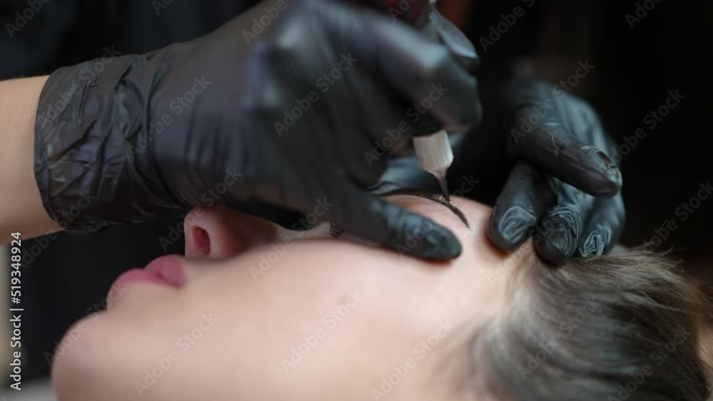 Micro blading tattooing of female eyebrow with microblading pen in beauty salon. Close-up face of Caucasian woman lying with professional tattoo master doing permanent makeup