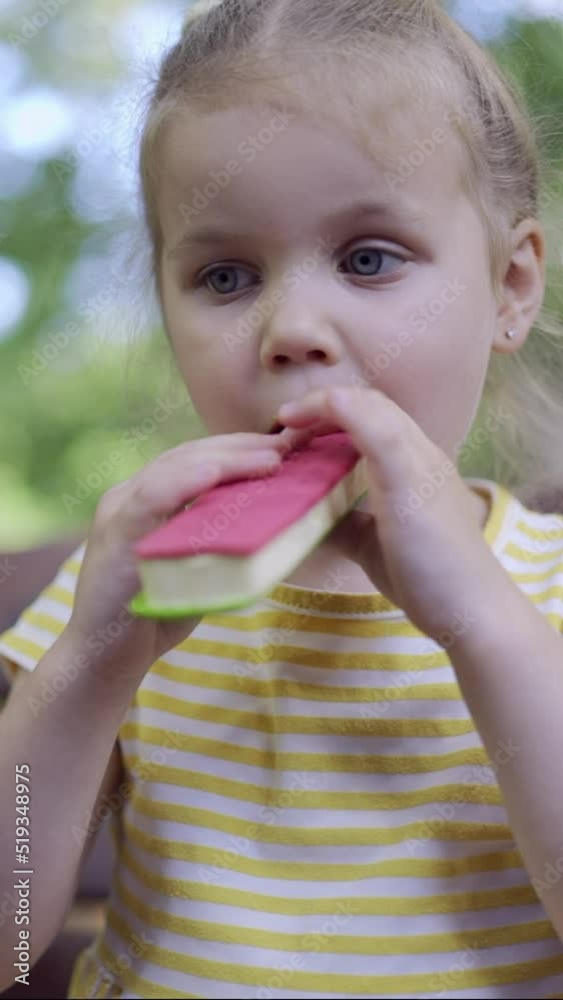 VERTICAL VIDEO: Closeup of cute little girl eats ice cream. Close-up of child girl sitting on park bench and eating icecream. VERTICAL VIDEO: Closeup of cute little girl eats ice cream. Close-up of child girl sitting on park bench and eating icecream.