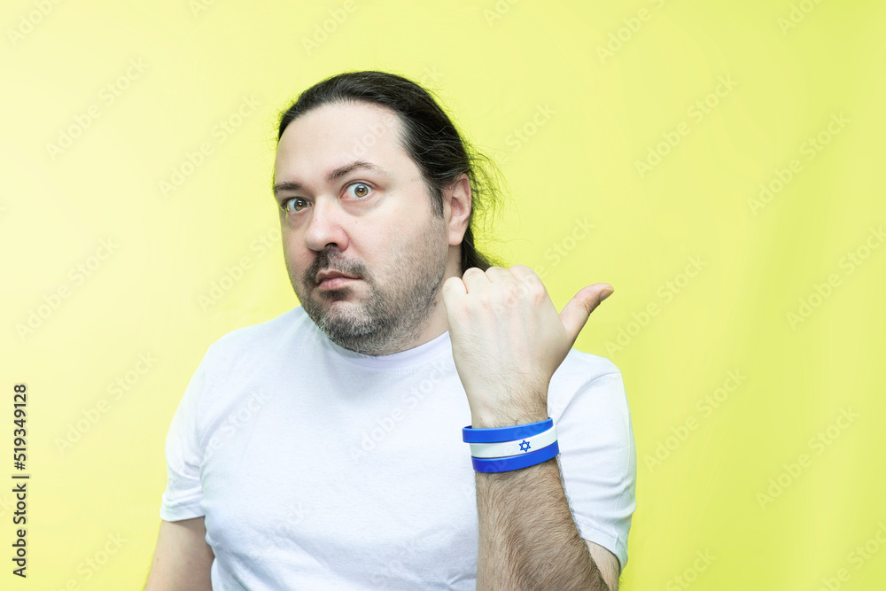 An adult, unshaven man in a T-shirt points his thumb to the side. A person draws attention to an empty space on the side. Bracelet in the colors of the flag of Israel. An adult, unshaven man in a T-shirt points his thumb to the side. A person draws attention to an empty space on the side. Bracelet in the colors of the flag of Israel.