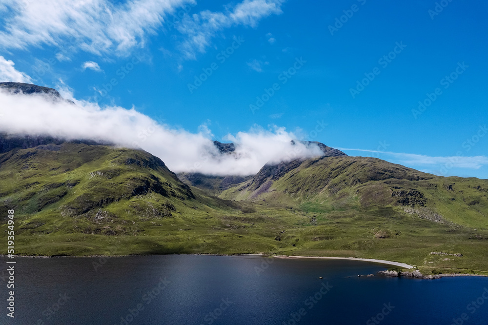 Green mountains under blue cloudy sky on a sunny warm day and lake with blue water. Nature scene in Connemara, Ireland. Irish landscape. Popular travel and sightseeing area.