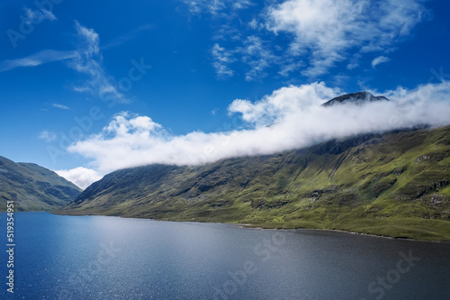 Green mountains under blue cloudy sky on a sunny warm day and lake with blue water. Nature scene in Connemara, Ireland. Irish landscape. Popular travel and sightseeing area.