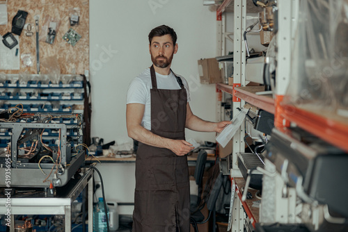 Man worker in uniform inspecting coffee machine in own workshop