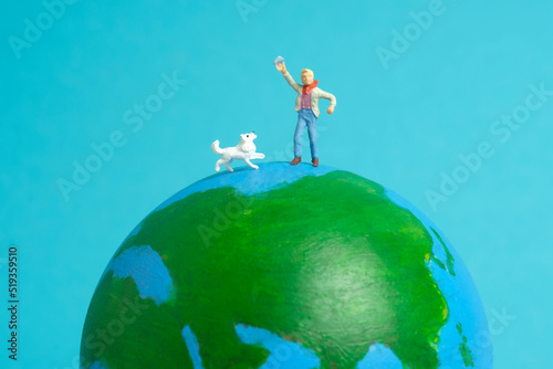 Miniature people toy figure photography. International kids day concept. A kid playing with dog above earth globe, isolated on blue background photo