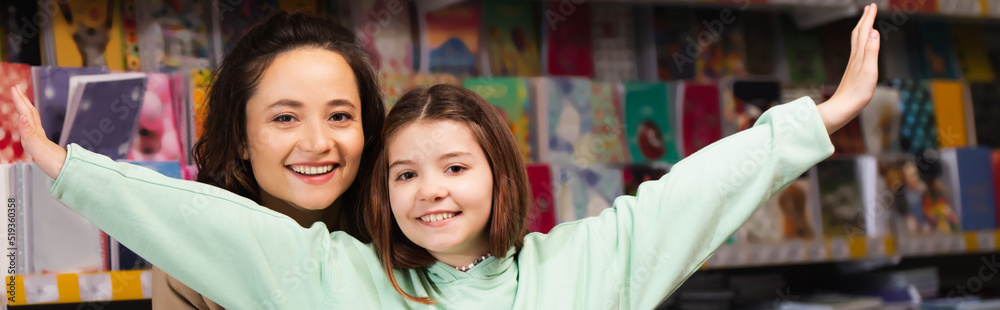 cheerful woman and excited girl with outstretched hands looking at camera in stationery store, banner. cheerful woman and excited girl with outstretched hands looking at camera in stationery store, banner.