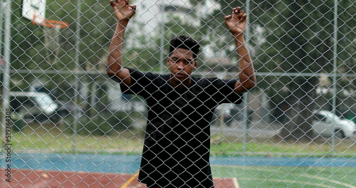 Upset African man leaning on metal fence. Angry black person shaking fence photo