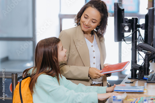 woman with daughter smiling at each other at cash desk in stationery store.