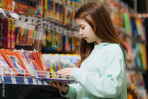 side view of girl holding pencil set near rack in stationery shop.