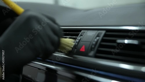 Car wash or car detailing studio employee wash the air vents in the car with a brush
