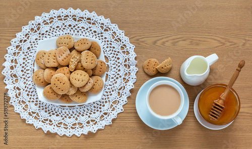 Top view of freshly baked homemade cookies on a handmade lace napkin  a cup of tea with milk and fresh honey on a wooden table. Home baking recipe. Close-up  flat lay  copy space