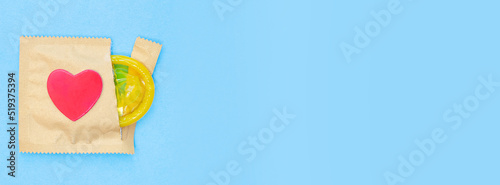 Banner with open pack with yellow condom and heart. Safe or risky sex. Blue background. Protection against diseases and infections. Copy space. Place for text. Top view. Flat lay.