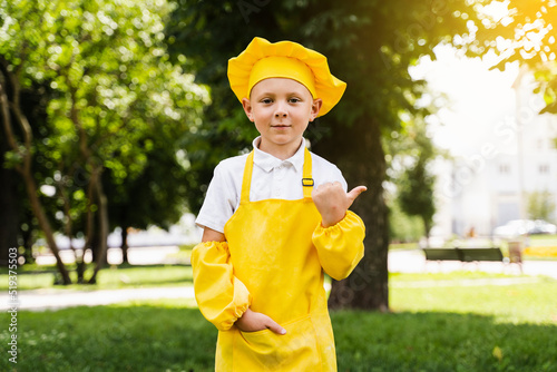 Point right. Handsome cook child in yellow chefs hat and apron yellow uniform pointing right side. Creative advert for food shop and cafe.