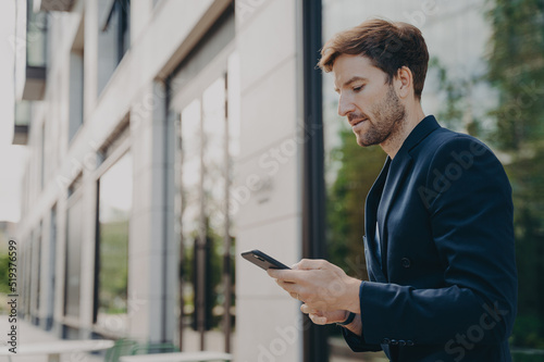 Handsome young man chatting and browsing web on his phone while standing outdoors