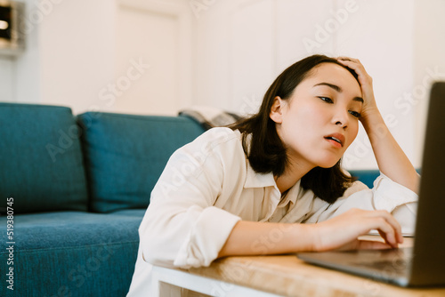 Young tired asian woman with laptop looking on screen