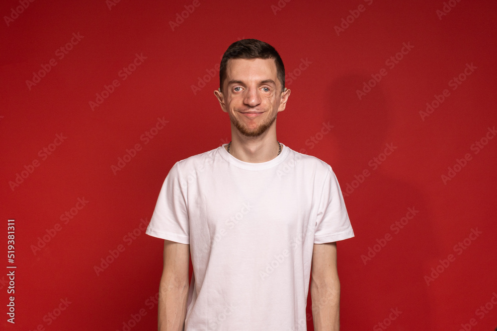 A young man in a white T-shirt stands against a red background and smiles A young man in a white T-shirt stands against a red background and smiles