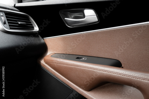 Car door handle inside the luxury modern car with brown leather interior. Switch button control. Modern car interior details. Orange perforated leather