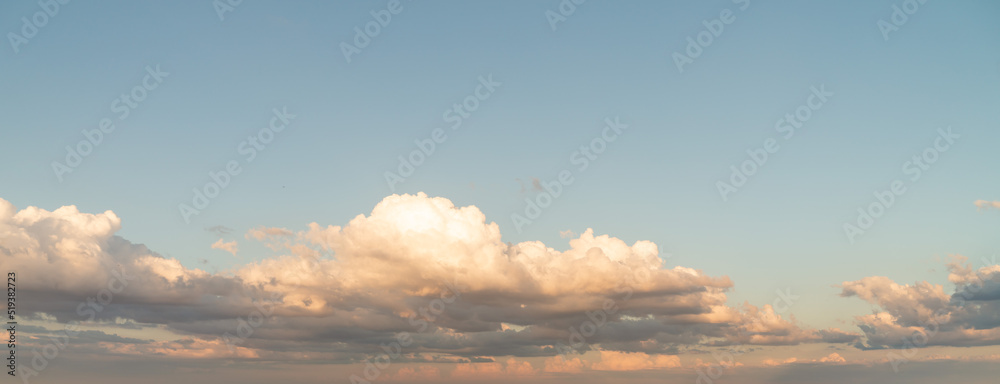 Obraz premium Beautiful panoramic sky replacement sunset background starting at the horizon with layers of fluffy white yellow and pink hued cumulus clouds on a blue sky background.