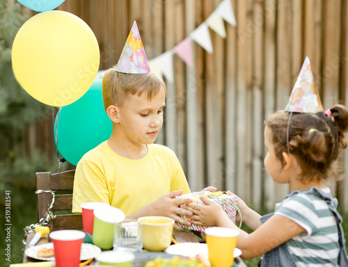 Cute funny nine year old boy celebrating his birthday with family or friends with homemade baked cake in a backyard. Birthday party for kids. His gets presents gift box.