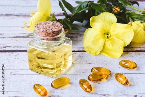 Evening primrose oil in bottle, softgels and flowers on wooden table