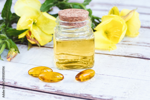 Evening primrose oil in bottle, pills and flowers on wooden table, Oenothera biennis essence photo