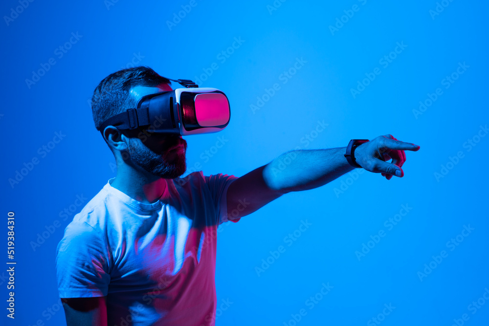 Man in white t-shirt wearing VR goggles using metaverse technology innovation in the virtual world. AR Concept over neon lighting and dark background. Virtual Reality experience. Future technology.
