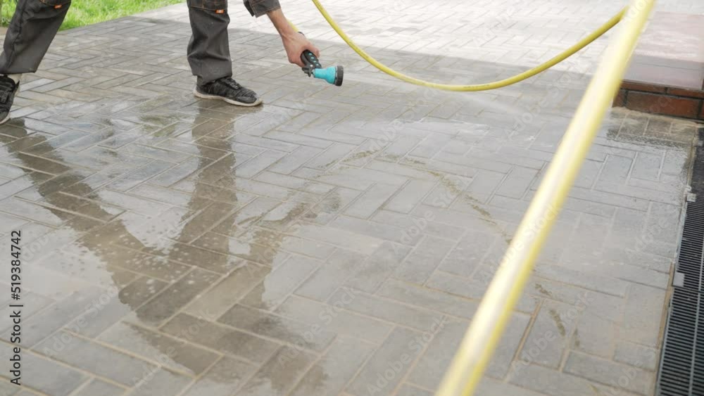 A man cleans pavement blocks with a high pressure water cleaner. The