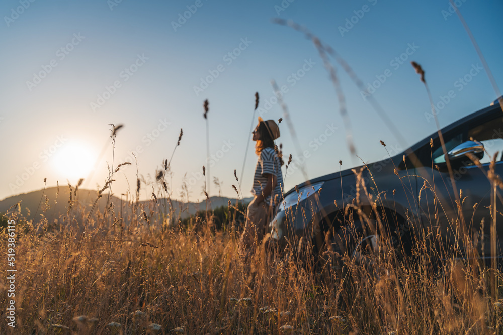 Young beautiful woman traveler enjoying the sunset in the mountains while traveling by car