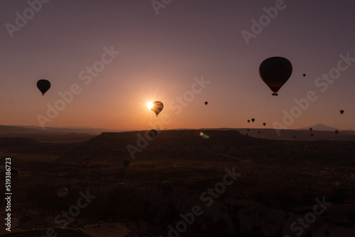 Sunrise in Cappadocia, with the sun eclipsed by a hot air balloon, with an orange and pink sky.