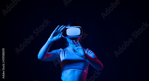 Young woman wearing vr headset and watching 360 videos in neon light. Girl toching virtual objects in vr glasses.