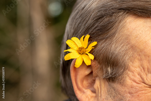 A Caucasian man has a yellow flower inserted behind his ear. Close-up with a blurred background.