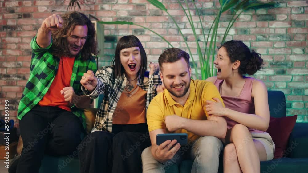 Good looking group of multiracial friends together watching a match on the smartphone at home on the living room they getting excited after their team getting the victory Good looking group of multiracial friends together watching a match on the smartphone at home on the living room they getting excited after their team getting the victory