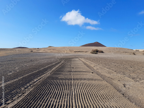 Perspective of sand rutted road in desert and volcanic landscape. Background of raked white sand. Clean beach sand texture with rake. Maintenance of beaches and coastline.