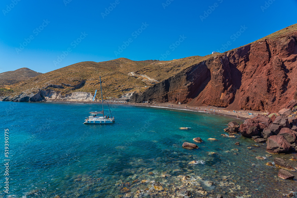 Beautiful scenery of red sand beach with a boat in Akrotiri village on Santorini, Greece