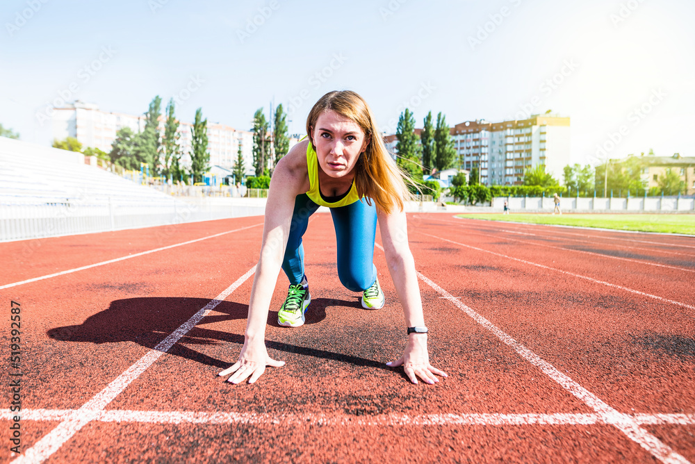 A young woman in the starting position for running on a sports track.