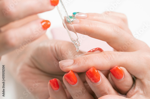 manicurist dripping anti-inflammatory oil on the cuticles of the client's fingers
