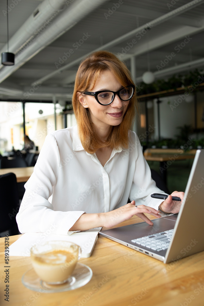 Business woman typing in the laptop in white shirt with eyeglasses at the table Business woman typing in the laptop in white shirt with eyeglasses at the table