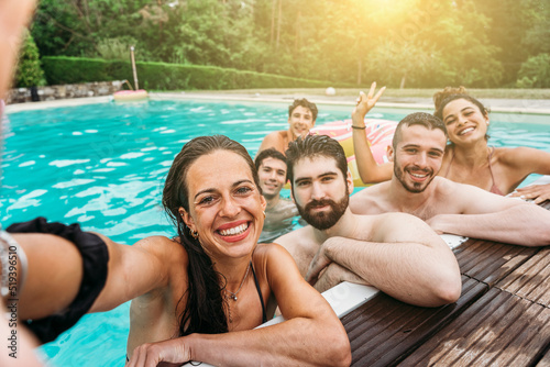 Smartphone self-portrait of a group of friends at the hotel outdoor pool during their summer vacation - Young people take a souvenir selfie photo in swimsuits having fun together in a relaxing moment