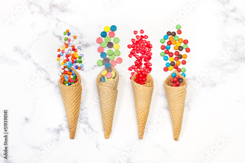 Caramelos dulces junto a conos de oblea de helado sobre un fondo de mármol texturado. Vista superior y de cerca. Copys pace