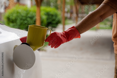 The man keeps a can for pouring gasoline from the canister into the car. Yellow watering can in the fuel holes. Gasoline collapse. Alternative fuelling method