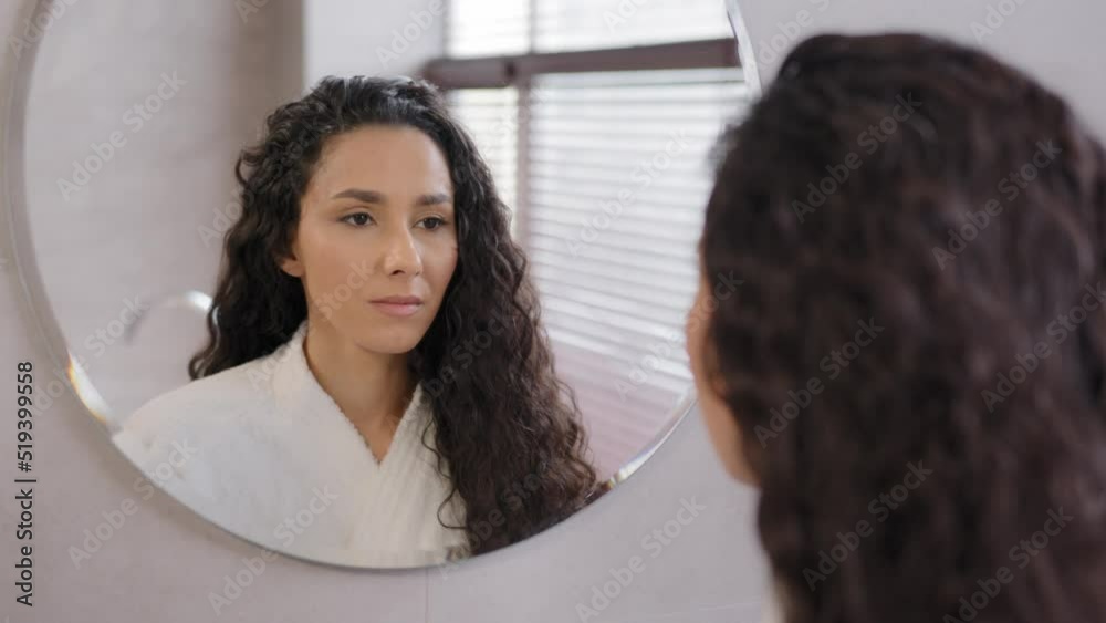 Close-up serious pensive young hispanic woman looking in mirror in bathroom contemplating future cute curly brunette girl in bathrobe admires reflection natural beauty daily morning routine concept